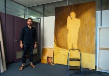 Christopher Bassi standing in an empty office next to a large yellow painting Christopher Bassi standing in an empty office next to a large yellow painting