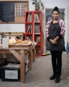 Naomi Hobson standing next to a wooden table and metal sink in her studio Naomi Hobson standing next to a wooden table and metal sink in her studio