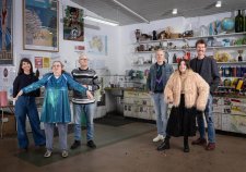 Two grounps of three people standing in a studio with walls and shelves filled with artworks Two grounps of three people standing in a studio with walls and shelves filled with artworks