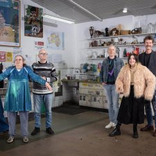 Two grounps of three people standing in a studio with walls and shelves filled with artworks Two grounps of three people standing in a studio with walls and shelves filled with artworks