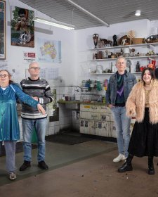 Two grounps of three people standing in a studio with walls and shelves filled with artworks Two grounps of three people standing in a studio with walls and shelves filled with artworks