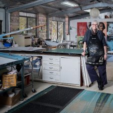 Alison Alder wearing a paint splattered apron, leaning against a bench in her studio Alison Alder wearing a paint splattered apron, leaning against a bench in her studio