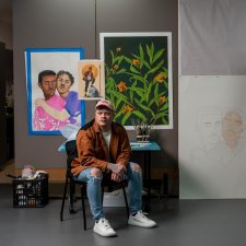 Dylan Mooney sitting on a chair in front of a wall with paintings and drawings Dylan Mooney sitting on a chair in front of a wall with paintings and drawings